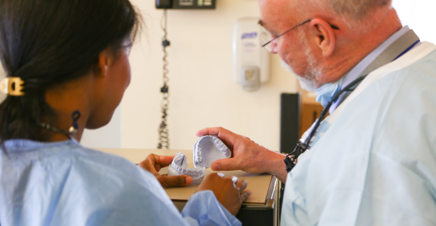 male elder teacher pointing to some dental molds with student